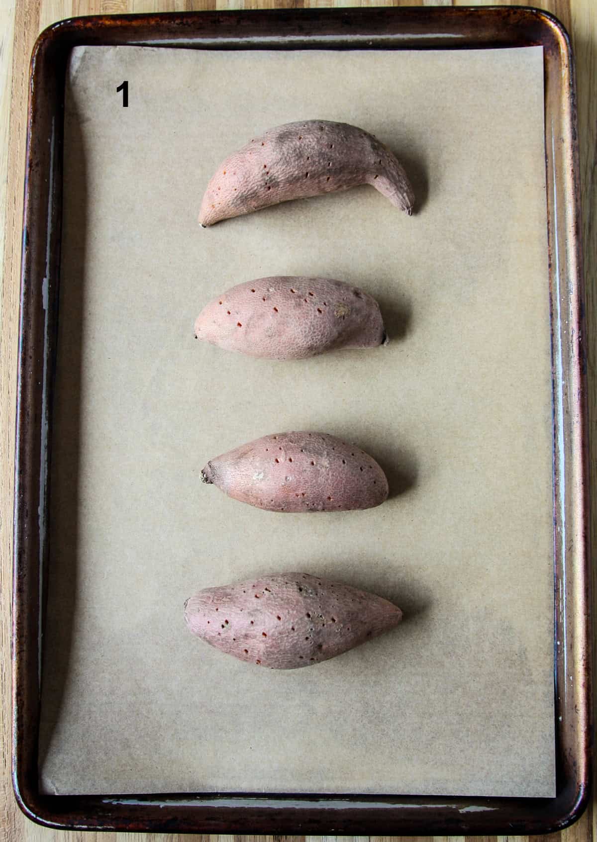Four small whole sweet potatoes on a baking tray.