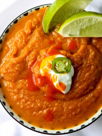 A bowl of southwestern pumpkin soup garnished with lime wedges.