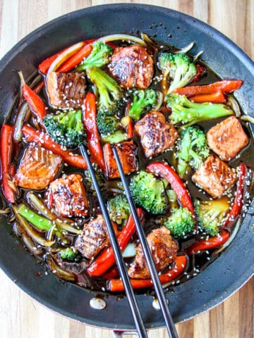 Salmon stir fry being cooked in a black skillet.