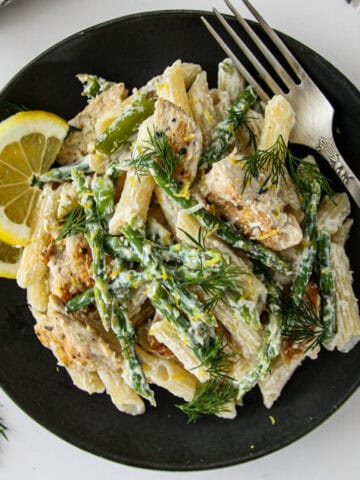 Asparagus and chicken pasta on a black plate.