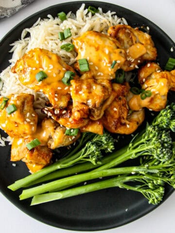Bang bang chicken on a bed of rice on a black plate.
