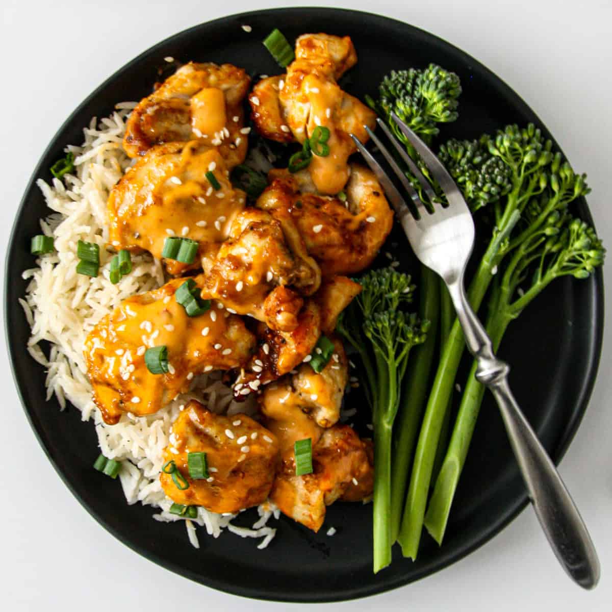 Bang bang chicken pieces on a bed of rice on a black plate.