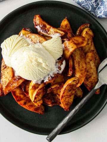 Air fried apple slices on a black plate, topped with vanilla ice cream.