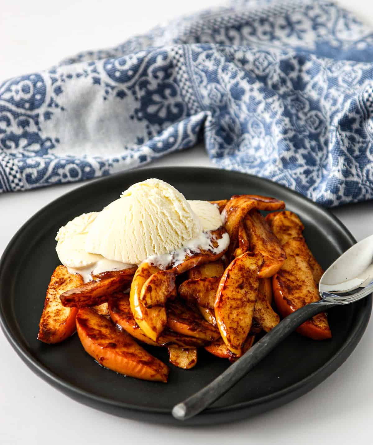 A black plate and spoon with air fryer apples and a scoop of vanilla ice cream.