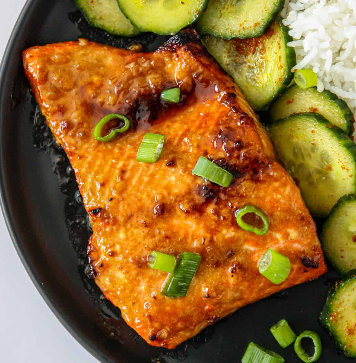 Miso butter salmon and cucumber salad on a black plate.